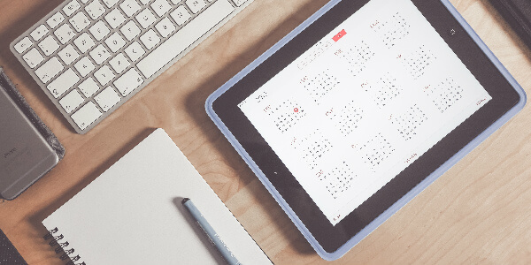 a tablet, keyboard, smartphone and a notepad sit on a desk with a calendar, signifying the importance of planning your group employee insurance now