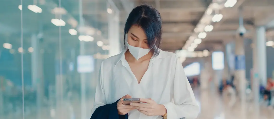 A businessperson looking at their phone while wearing a mask in an airport