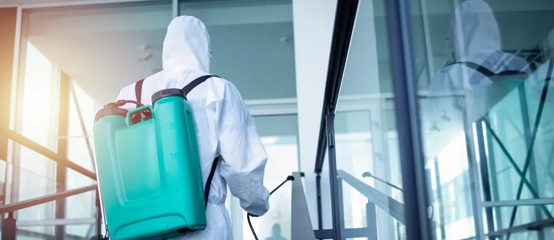 A person in a biohazard suit spraying pesticide inside a building